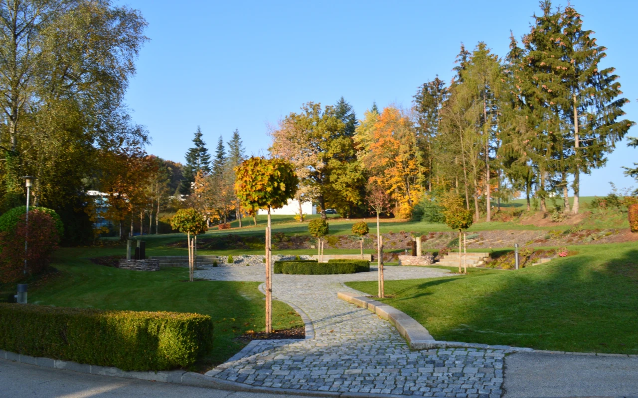 Bild Gepflasterte Wege führen durch den liebevoll angelegten Klinikpark mit Bäumen, Hecken und gepflegten Grünflächen in herbstlicher Atmosphäre.
