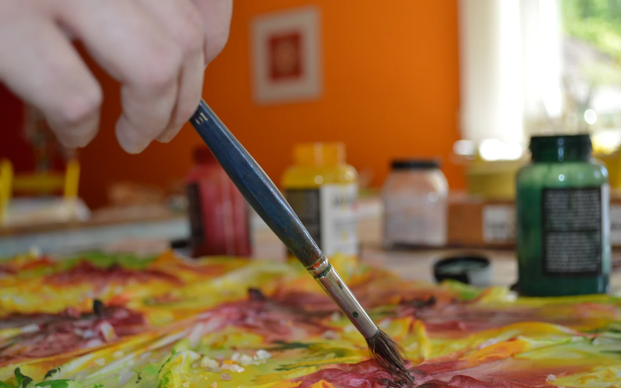 Bild Eine Person gestaltet mit einem Pinsel ein farbenfrohes Seidentuch – Symbol für Kreativität und Kunsttherapie in der Rehabilitation.