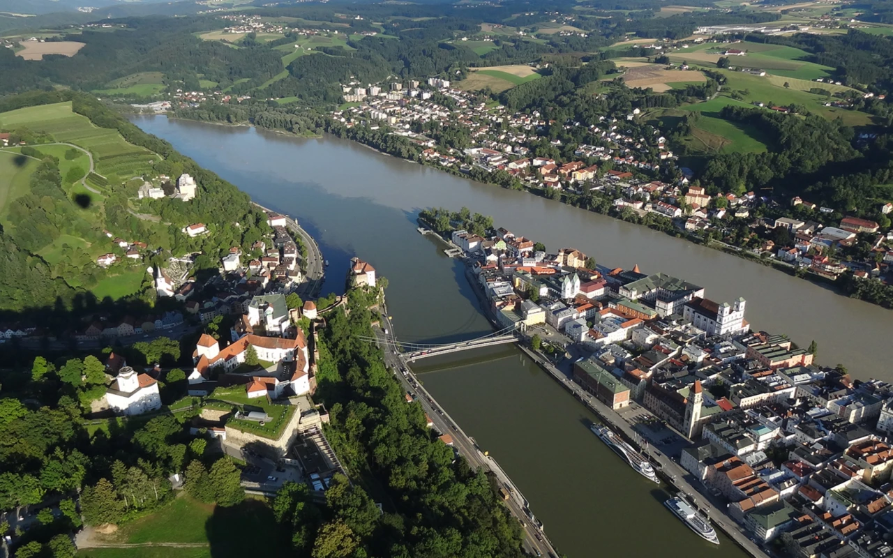 Bild Luftaufnahme der Dreiflüssestadt Passau mit Donau, Inn und Ilz, der Altstadt, der Veste Oberhaus und der Luitpoldbrücke in einer grünen Hügellandschaft.